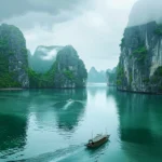 Ha Long Bay in Vietnam with emerald green waters, limestone cliffs covered in lush greenery, and traditional boats under misty skies